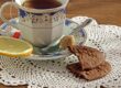 Teacup with tea, lemon slice, sugar cube, and chocolate biscuits on a doily.